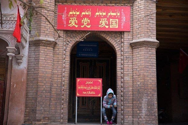طفل يجلس بالقرب من مدخل مسجد مع لافتة كتب عليها "أحب الحفلة ، أحب البلاد" في منطقة مدينة كاشغر القديمة في منطقة شينجيانغ شمال غرب الصين.